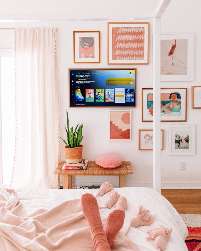 Discovery Plus on TV as a part of a gallery wall with feet in the foreground on a bed