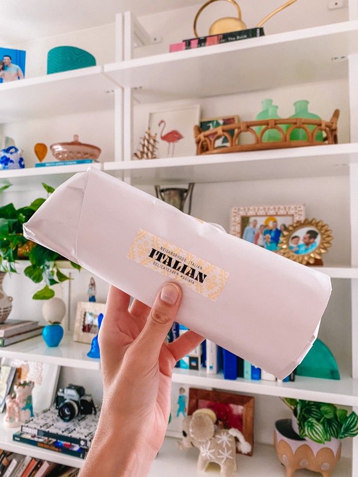 Wrapped Italian sandwich held in front of bookshelves