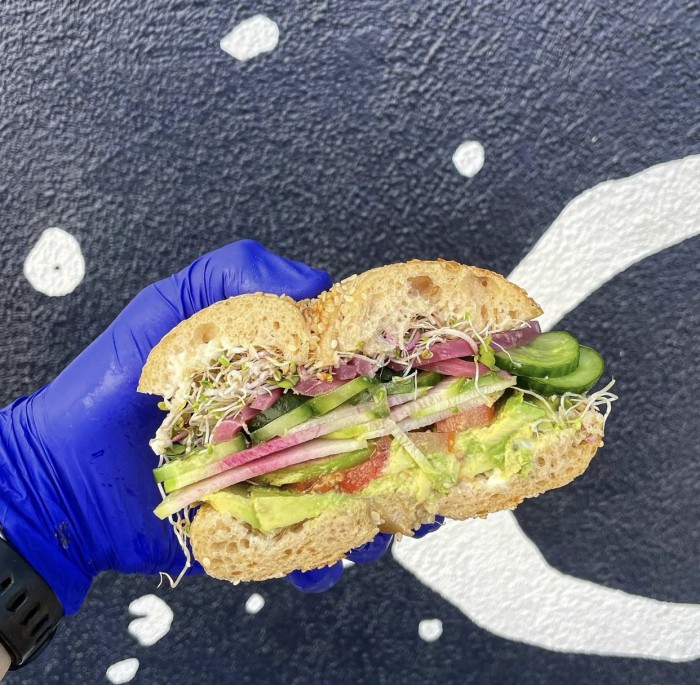 Vegetarian bagel sandwich held by hand in a blue glove