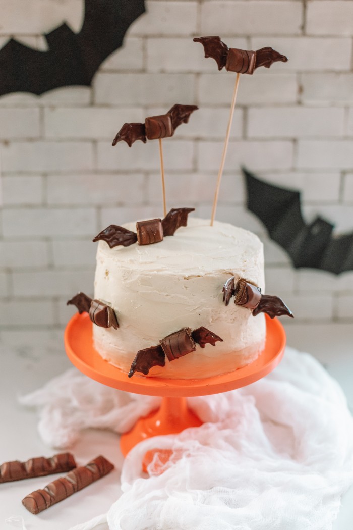 White cake with chocolate bats on it on an orange cake stand