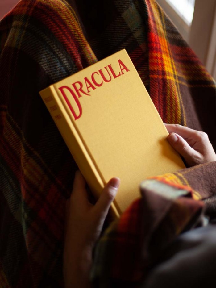 Hands holding Yellow Dracula book over a plaid blanket