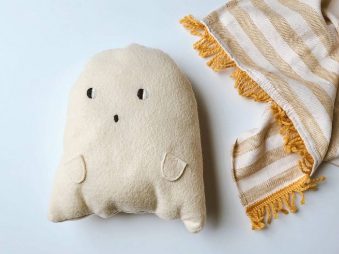 Plush ghost pillow next to a striped blanket on white background