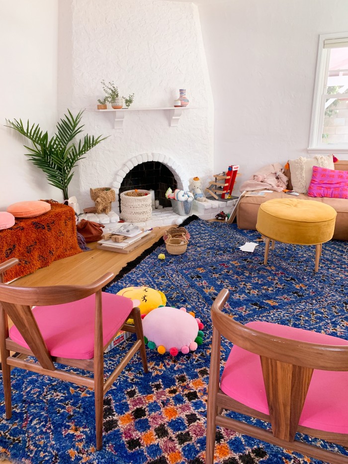 Messy living room with blue rug and pink dining chairs