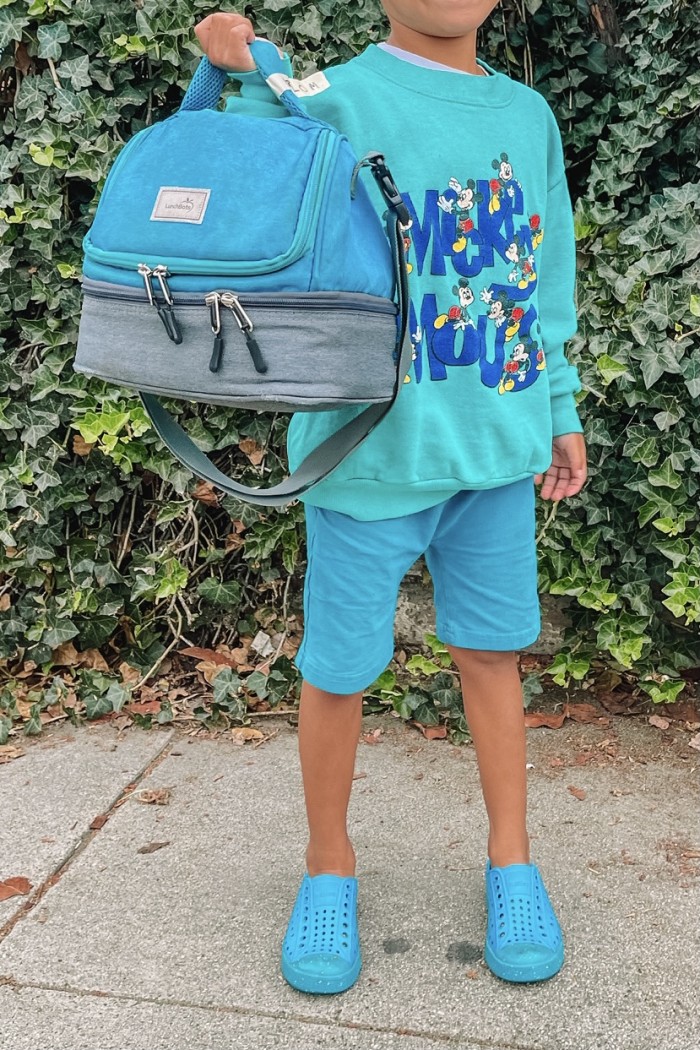 child wearing turquoise blue holding a lunch bag