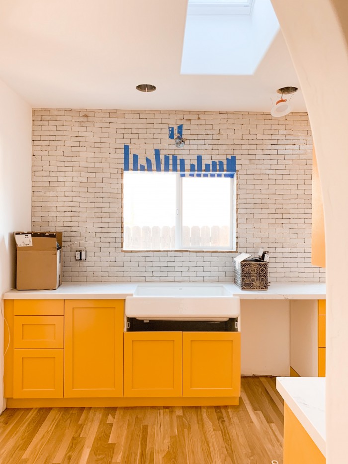 Yellow orange kitchen cabinets with white zellige tile above