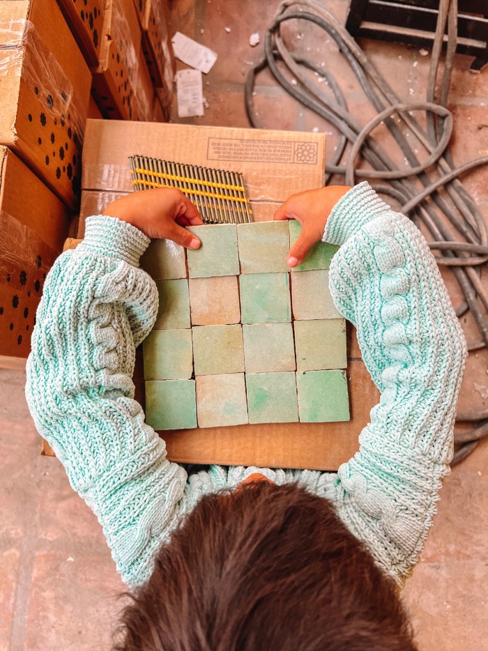 Child holding mint green zellige tile in a mint green sweater