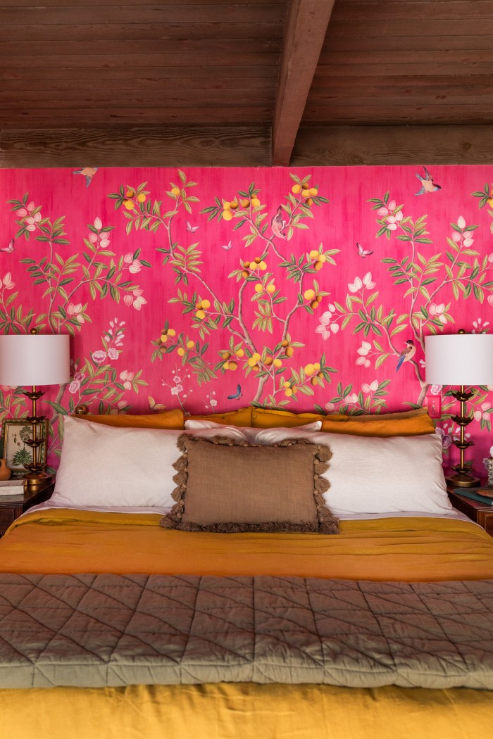 mustard and olive bed with pink wallpaper behind and lamps on nightstands
