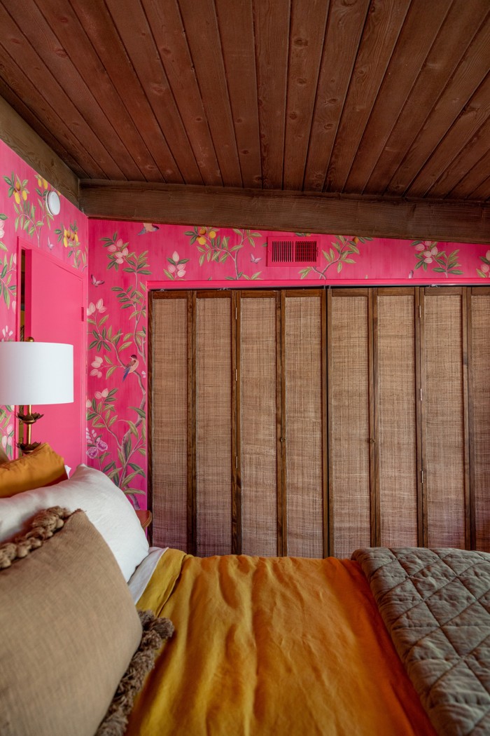 rattan bifold closet doors with pink chinoiserie wallpaper and bed in front