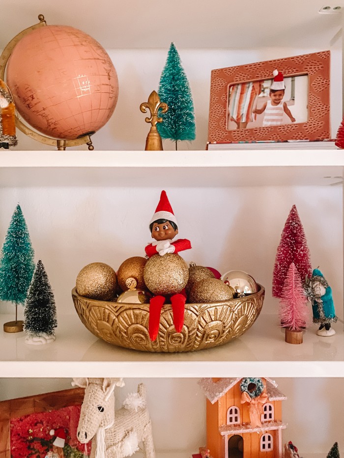 Elf on the Shelf sitting in bowl of ornaments on shelf