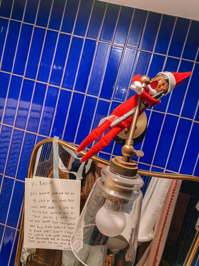 Elf on the shelf hanging on sconce in blue bathroom