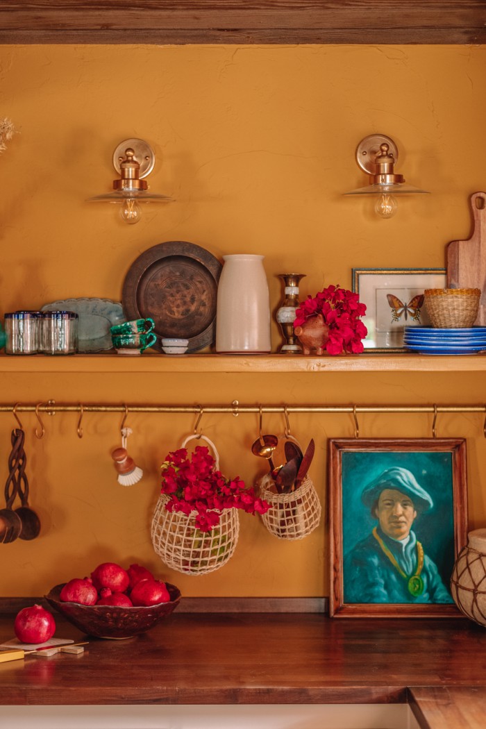 yellow kitchen with brass pot rail and portrait painting on butcher block counters