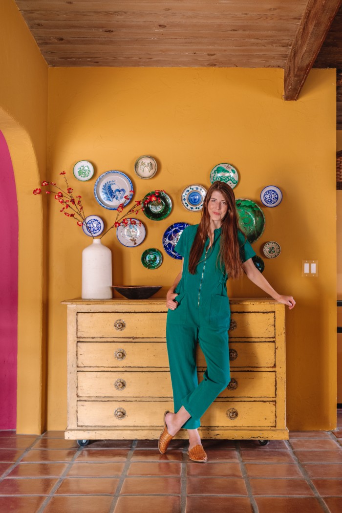 woman in green jumpsuit standing in front of yellow wall with decorative plates