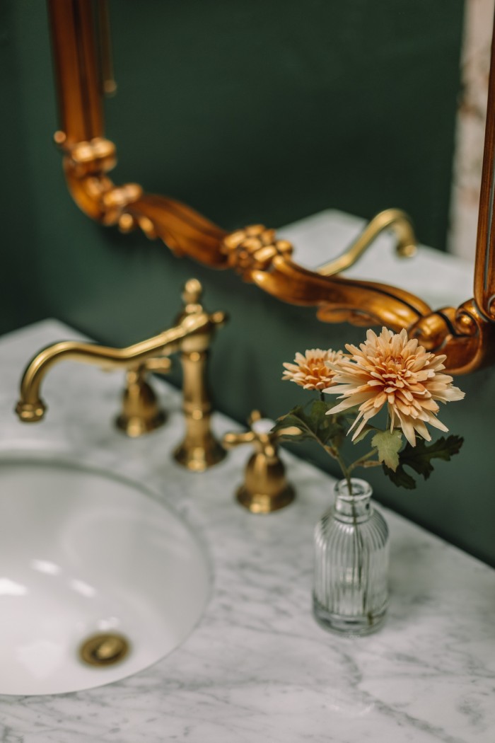 Brass faucets on marble vanity in green bathroom