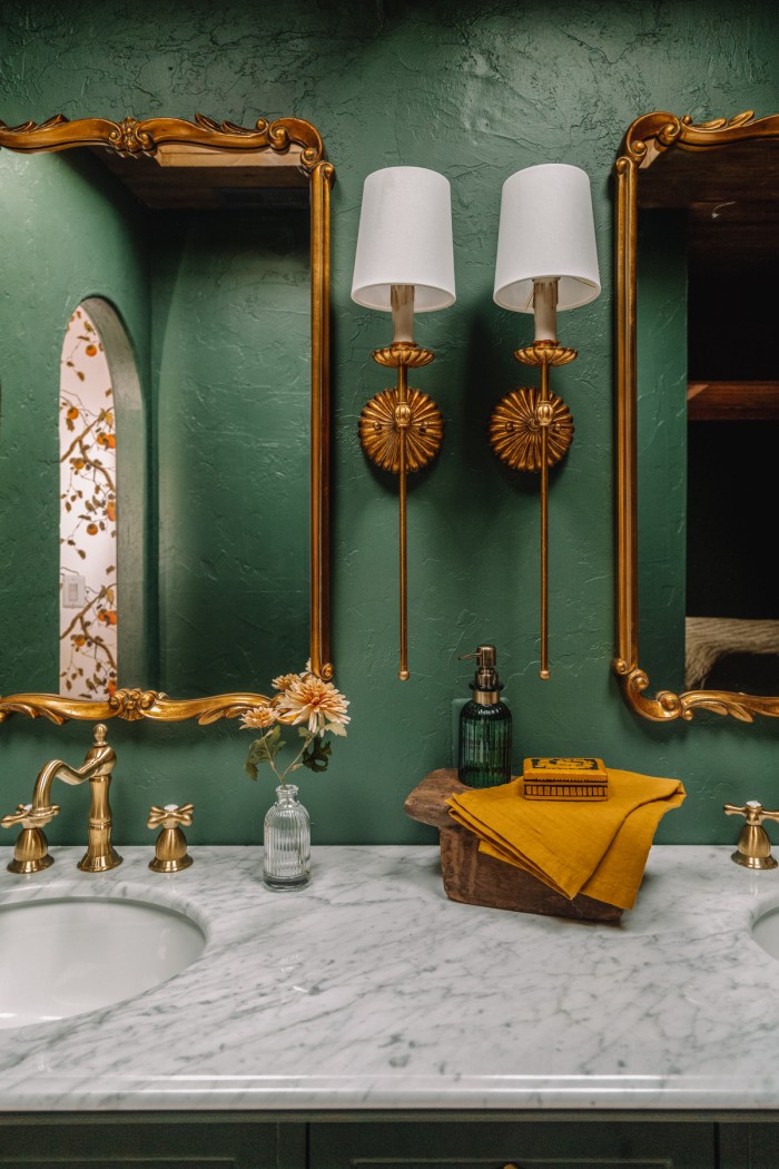 Green bathroom with brass sconces and mirrors