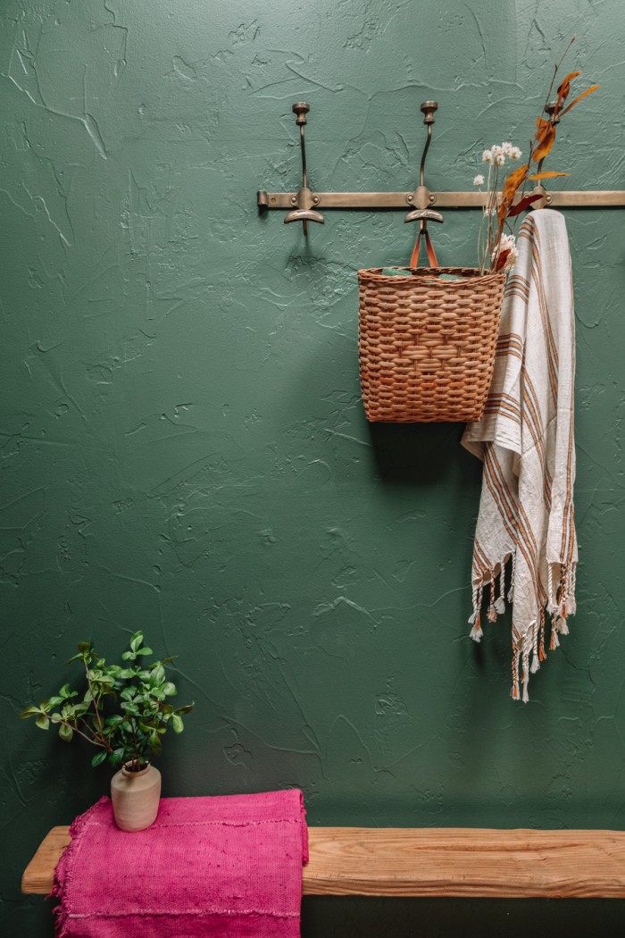 Bench on green wall with brass hooks above