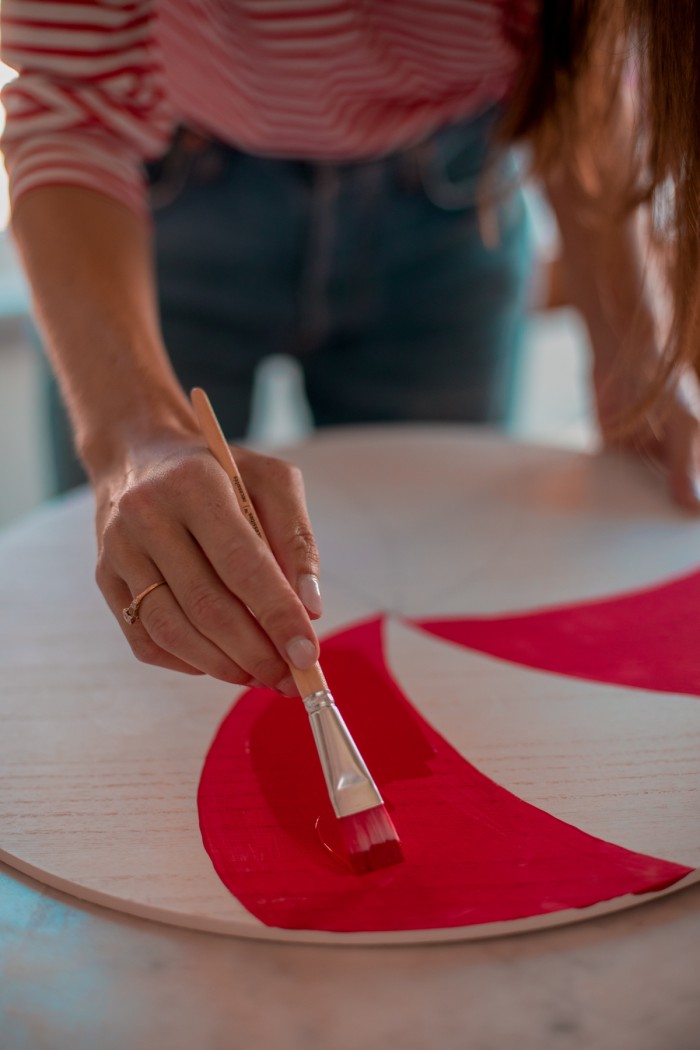 Hand paining a white board with red swirls to make it look like a peppermint. 