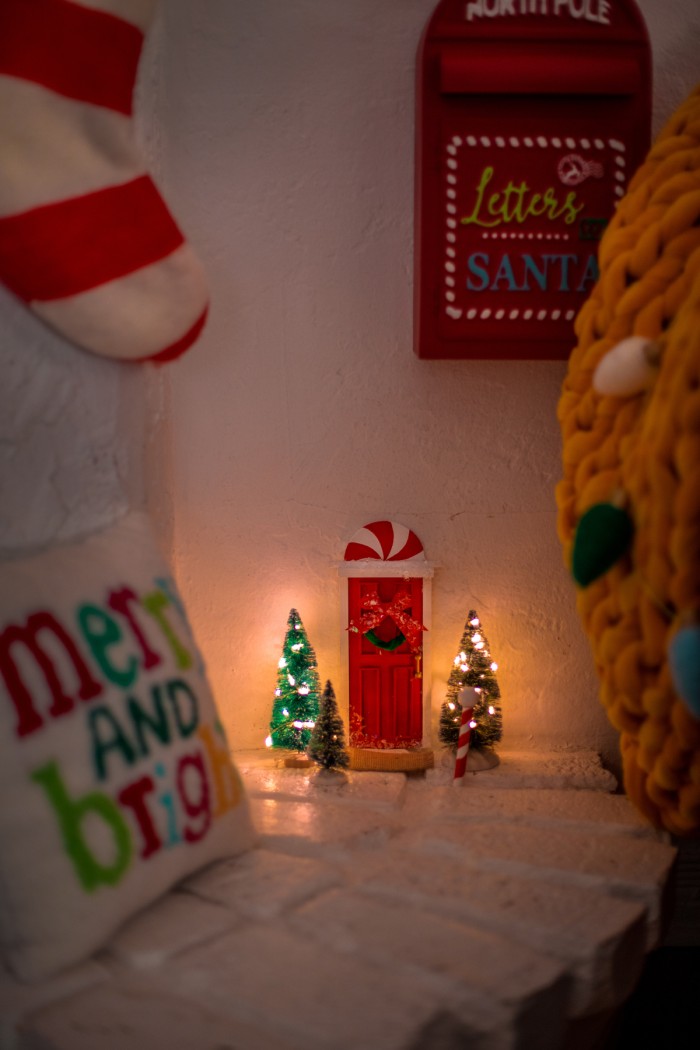elf on the shelf door next to a fireplace with small trees surrounding it to create a scene of a front door. 