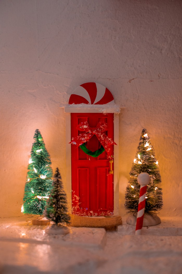 Elf door with small trees around it, a doormat and a north pole. 