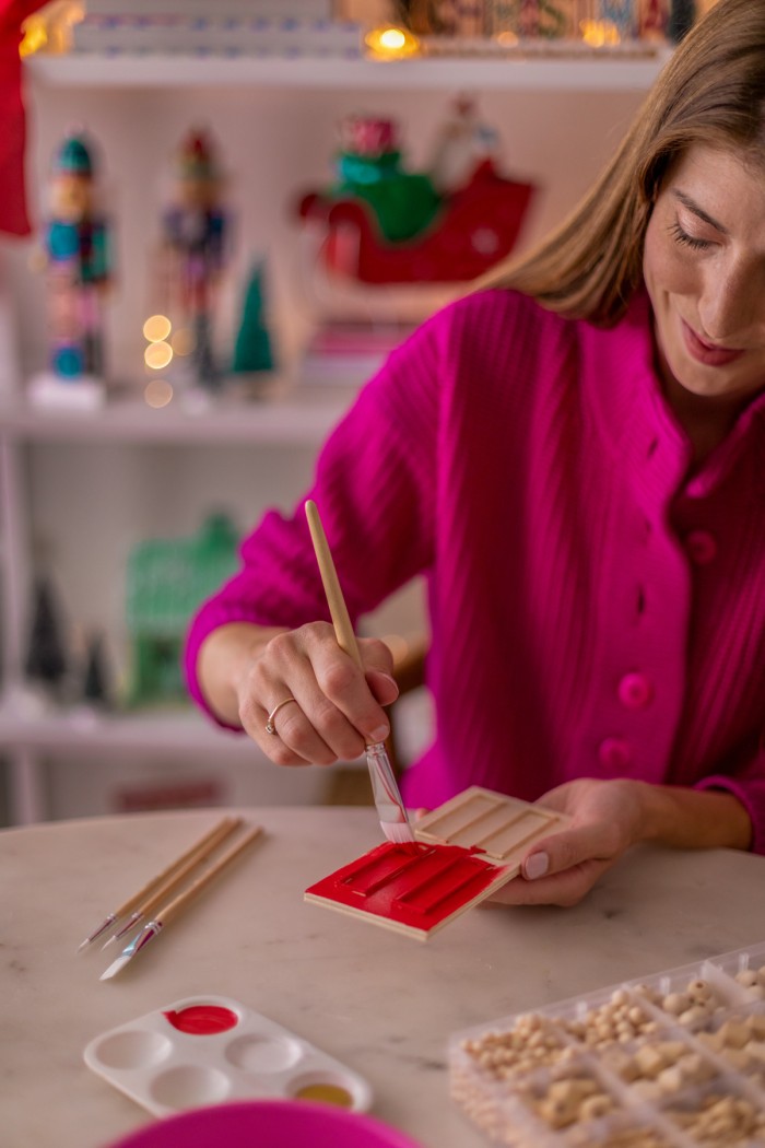 Woman holding a paint brush and painting a mini door red. 