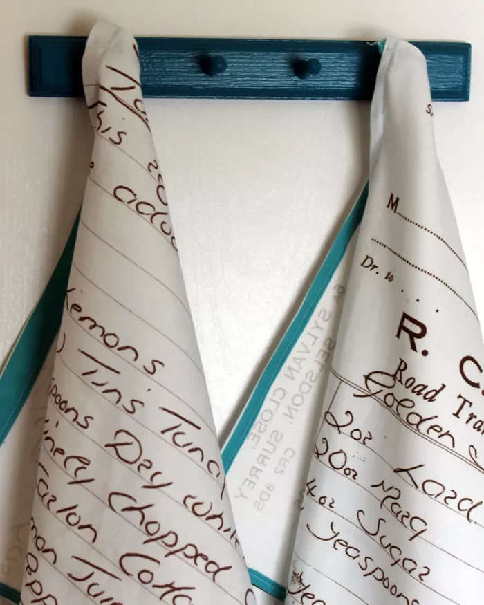 Two tea towels hanging up with hand writing on them. 