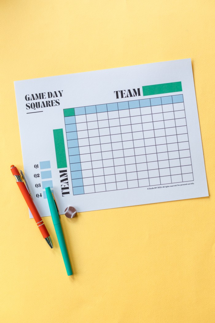 Paper with football game squares and pens next to it on a yellow background. 