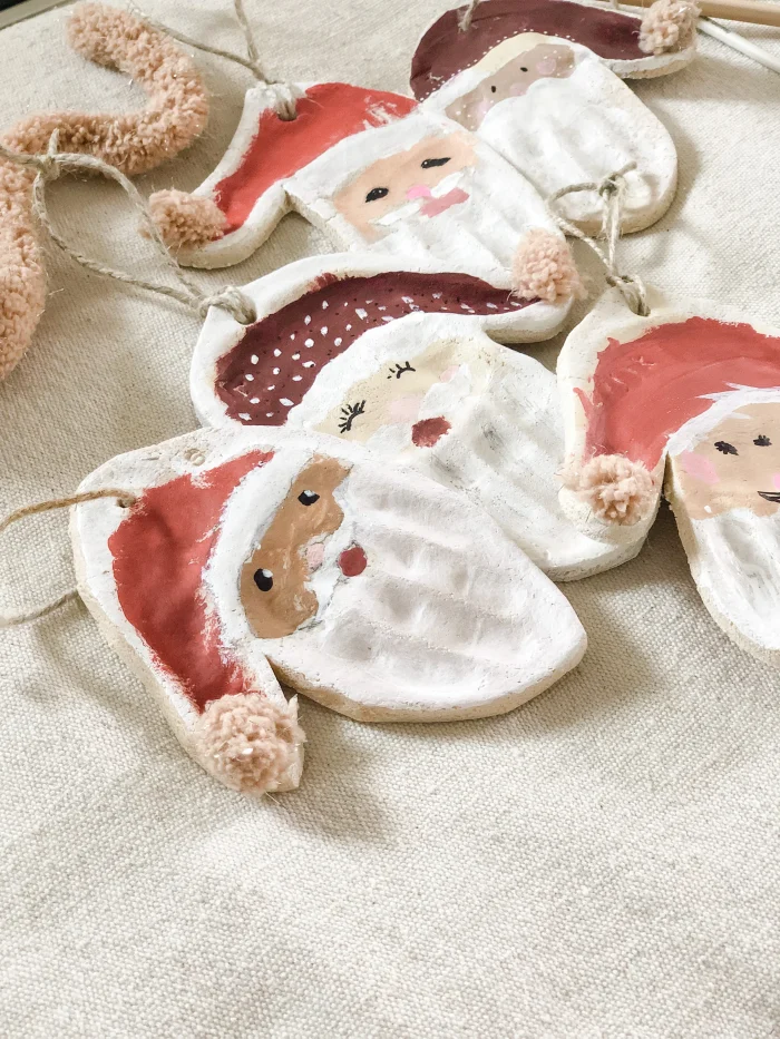 Christmas ornaments in the shape of santa's head on a tan cloth. 