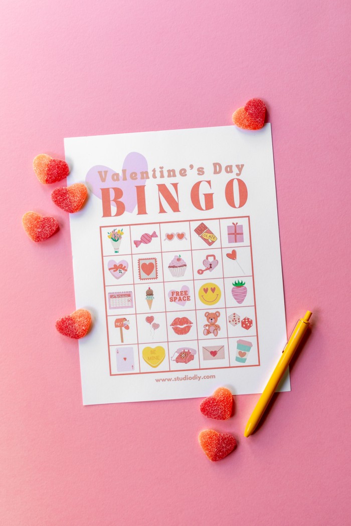 Printed Valentine's day bingo on a pink background with heart gummies scattered on top. 