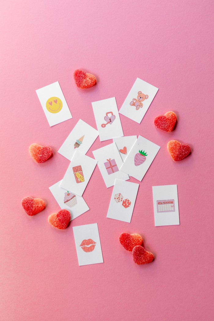 Calling cards cut out for bingo places on a pink background next to heart shaped gummy candies. 