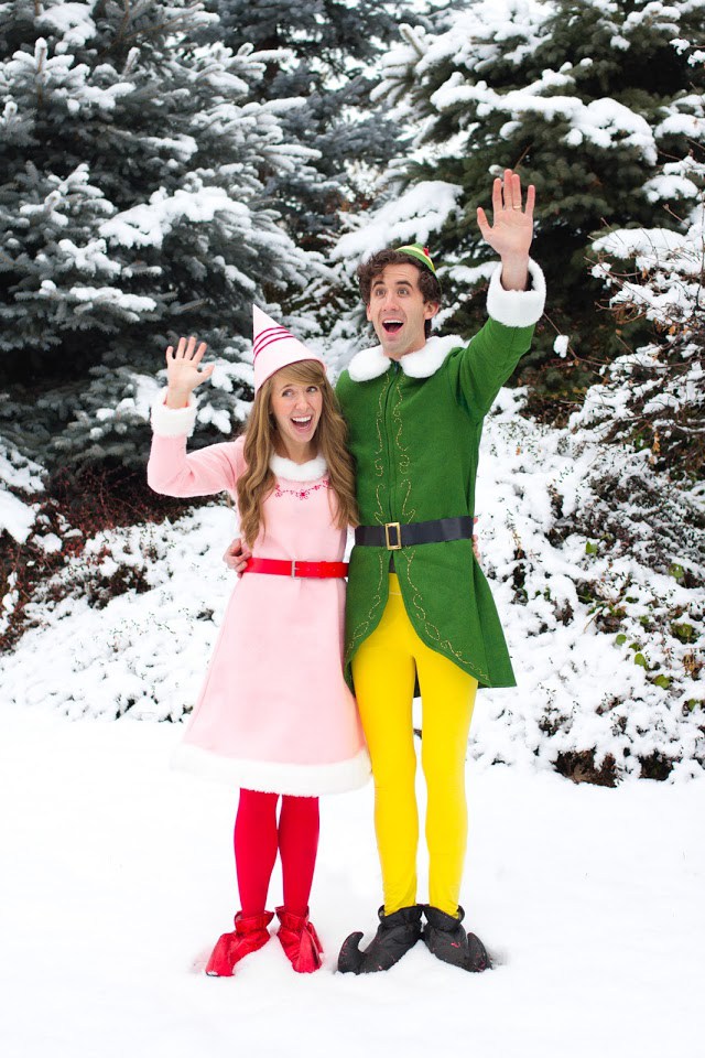 Man and woman dressed as elves and waving while standing outside in the snow. 