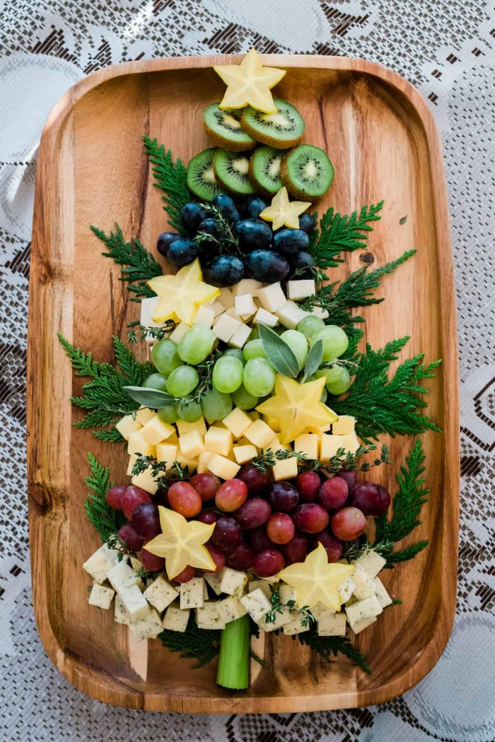 Grapes and cheese layered on a wooden board in the shape of a tree. 