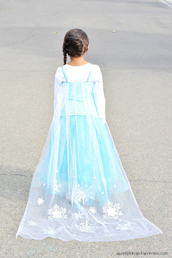 Girl standing with her back to the camera, dressed with a blue dress and long white veil with snowflakes on it. 
