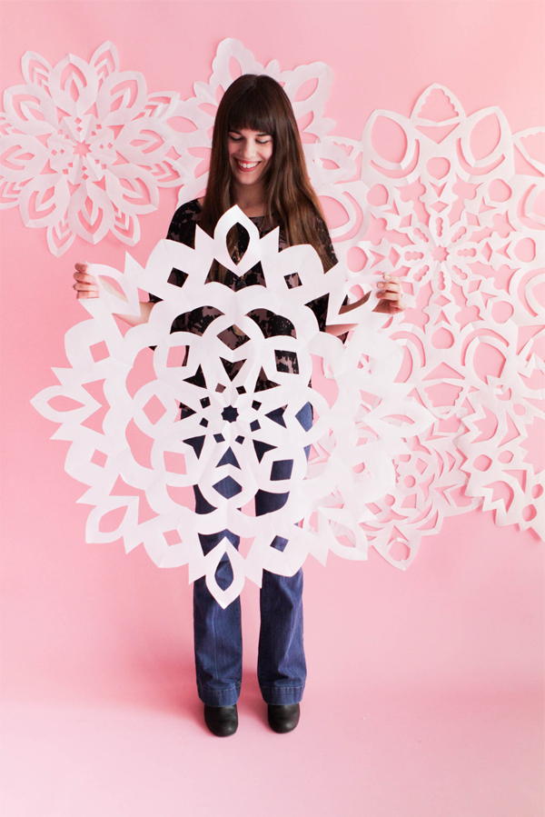 Woman holding a giant snowflake with a pink background.