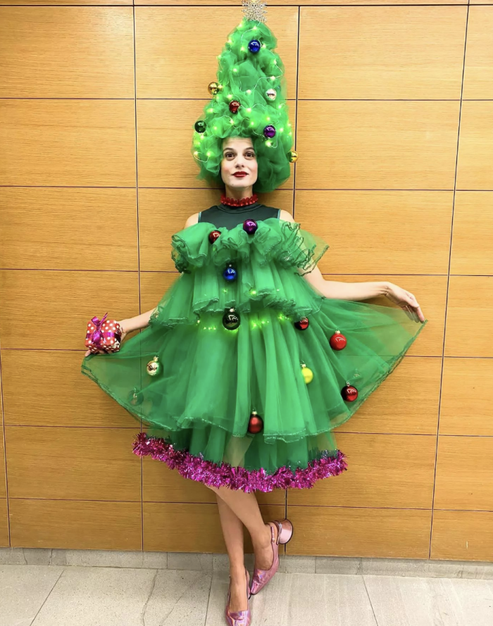 Woman standing in front of a wall wearing a Christmas tree costume made of tulle. 