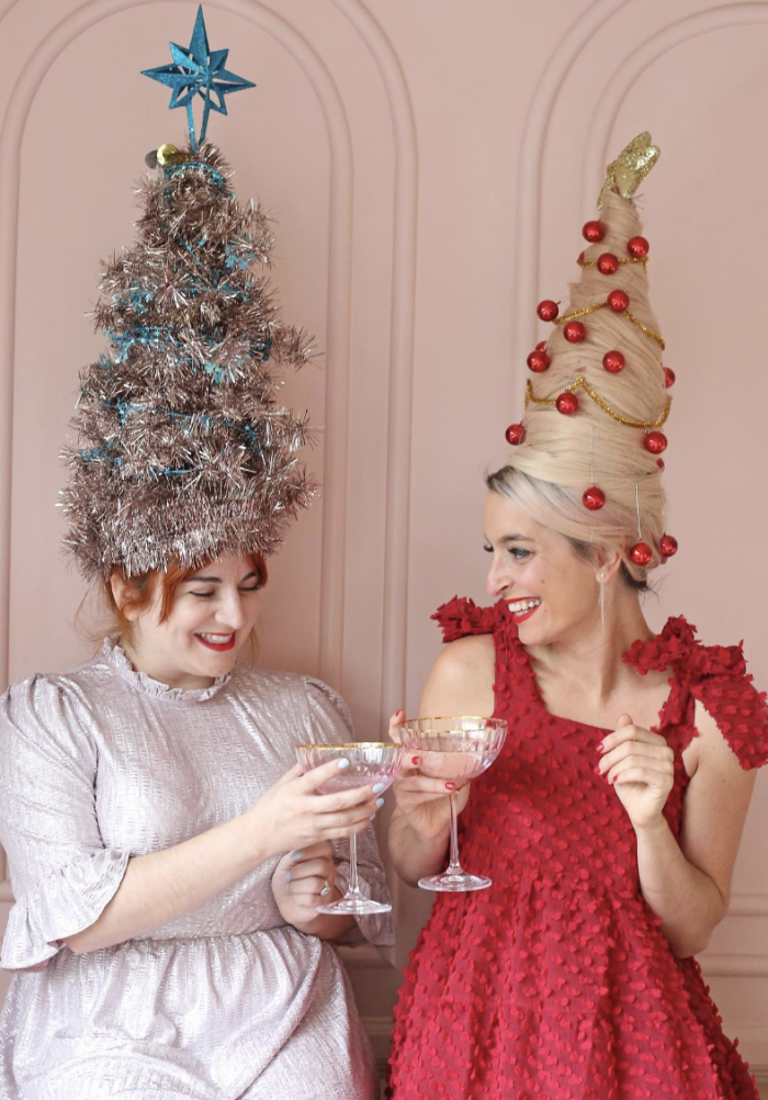 Two woman holding drinks with large tree-shaped wigs on their heads. 