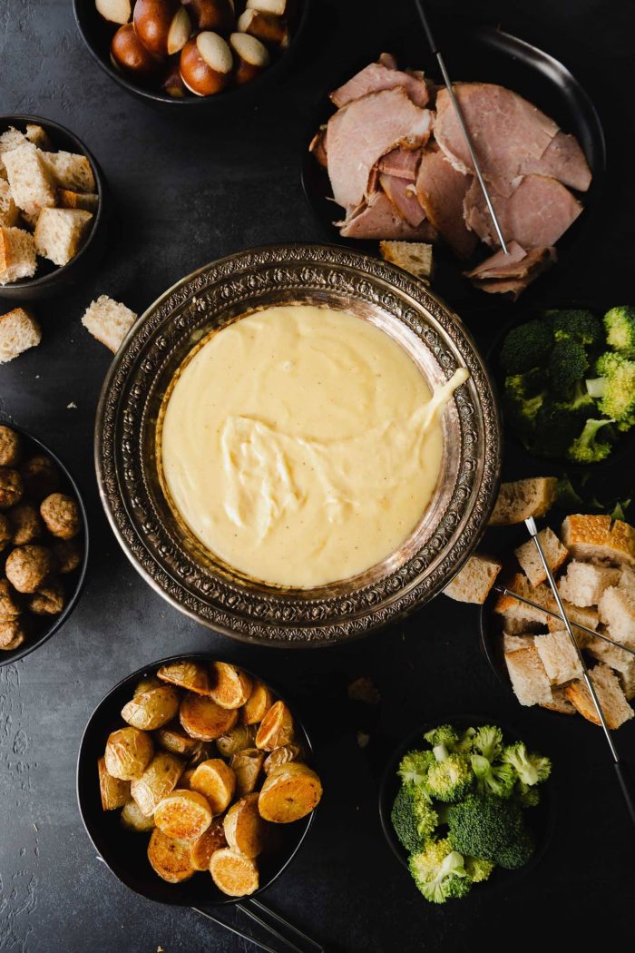 Cheese fondue surrounded by sides on a black background. 