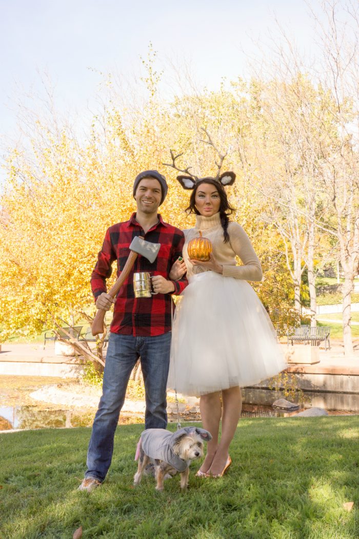 A man, woman and dog dressed up as a lumberjack, deer, and mouse and standing outside. 