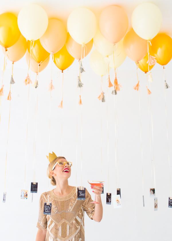 Woman looking up at golden balloons with photos tied to them at the bottom. 