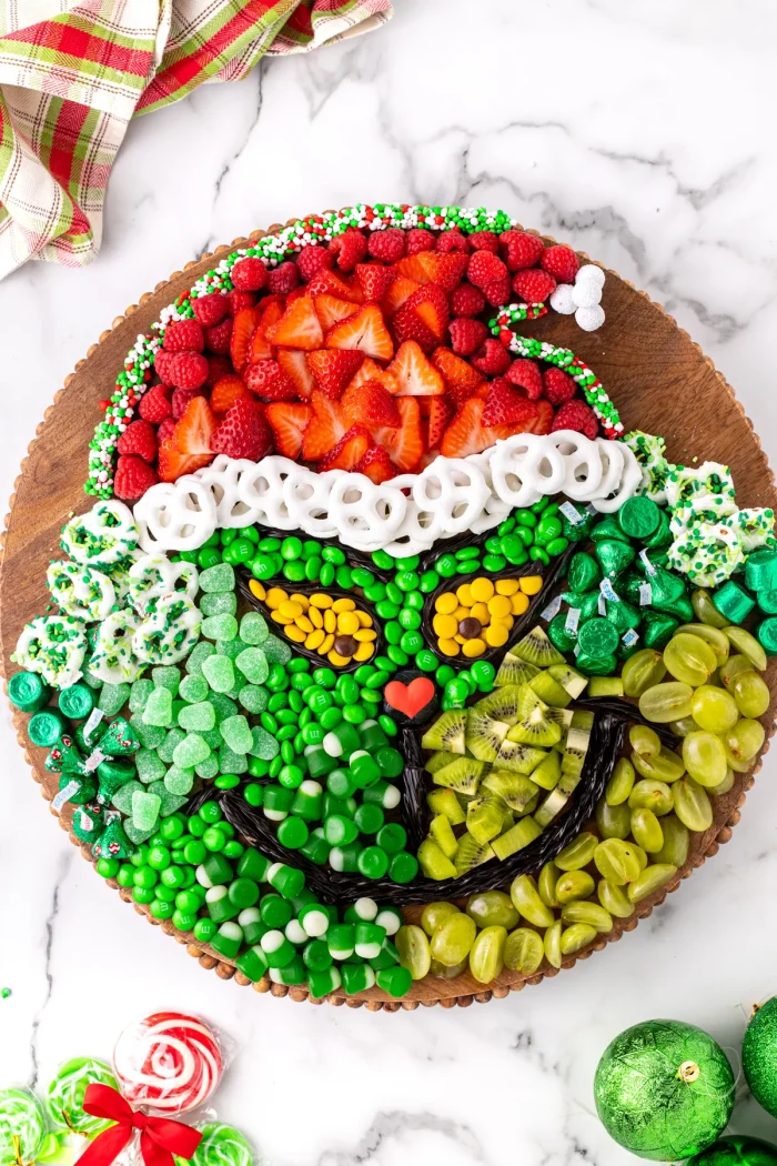 Fruits and candies in the shape of the Grinch on a wooden board. 