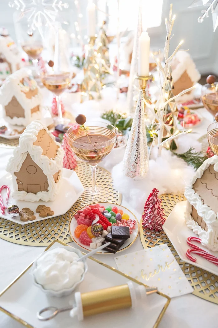 Table with assembled ginger bread houses and cocktail glasses with candy on plates. 