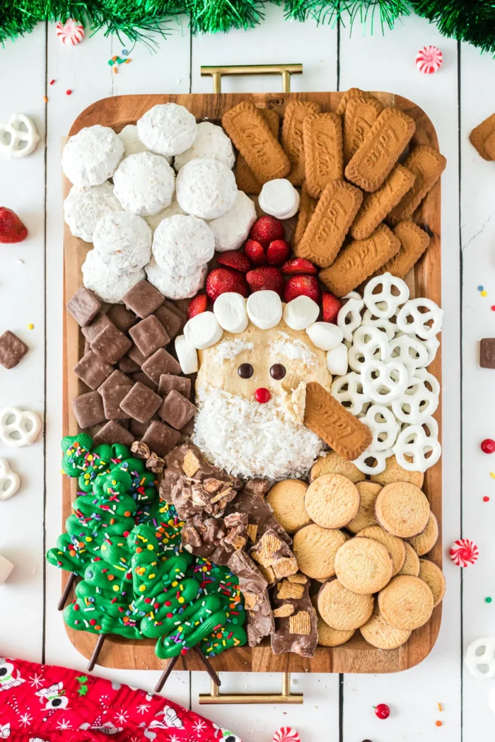 Santa cheesecake ball surrounded by cookies and pretzels on a wooden board. 