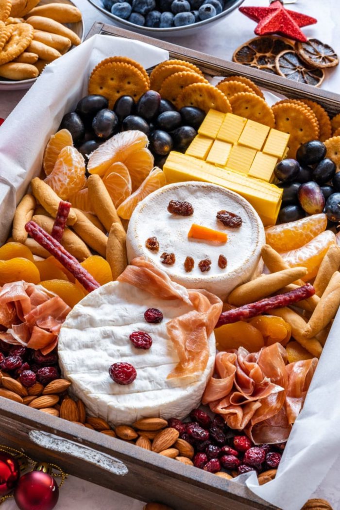 Snowman made of brie surrounded by crackers, meats and fruit. 