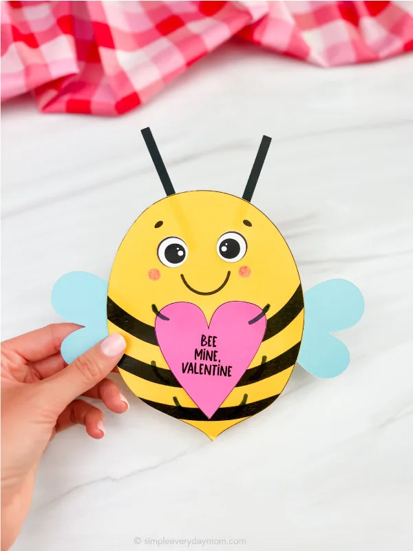 Hand holding a valentine shaped like a bee out of paper. 