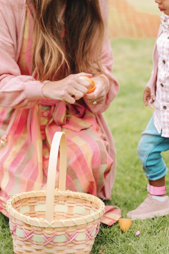 Woman opening a plastic egg while kneeling in front of a woven easter basket. 