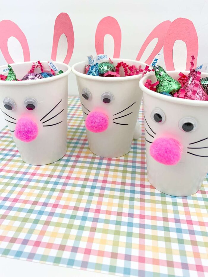 Three white paper cups with bunny faces on them and filled with candy. 