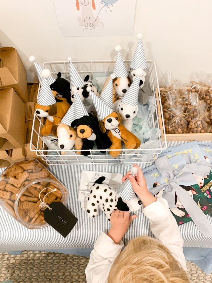 Child's hands placing a hat on a stuffed dog, with more stuffed dogs in a basket. 