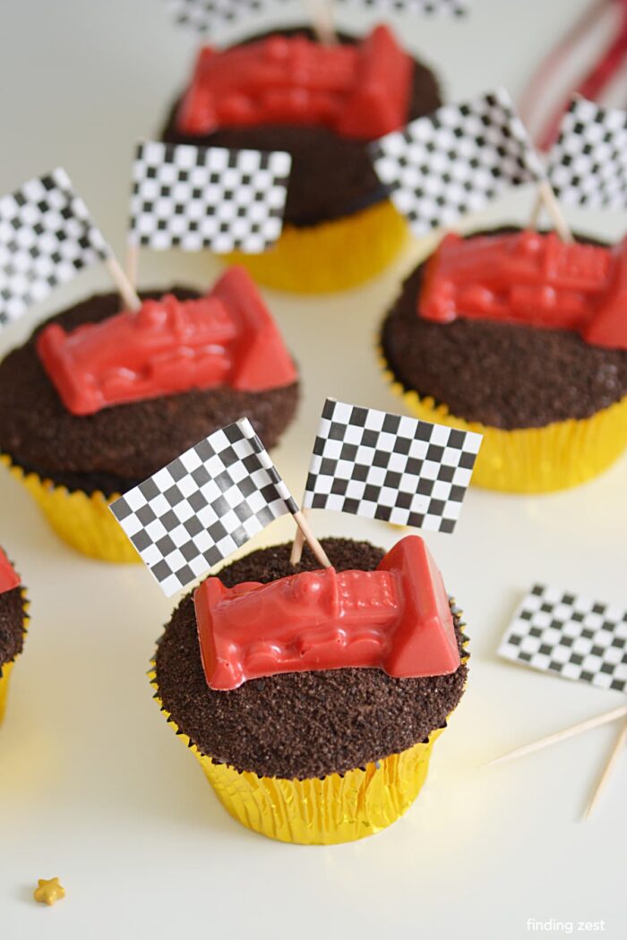 Cupcakes topped with crushed cookies and a race car with flags. 