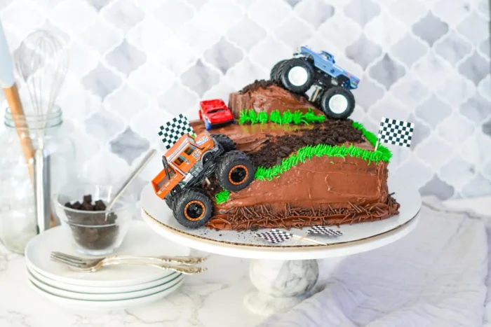 Chocolate cake with two monster trucks on it. 