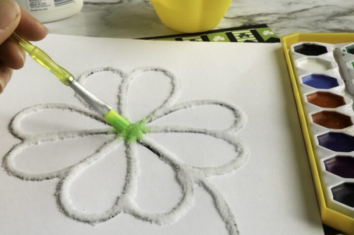 Shamrock made from glue and salt on a paper with a hand painting it green. 