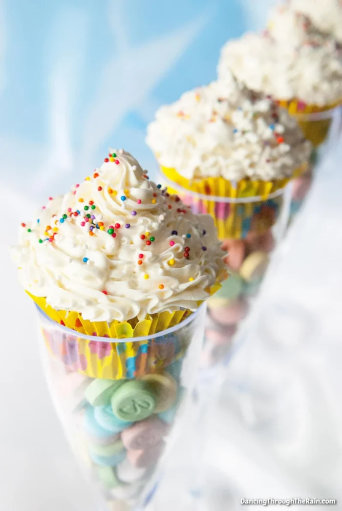 Champagne glasses with candies in the bottom and cupcakes on top. 
