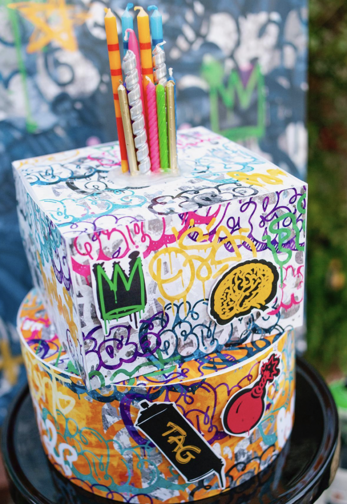 Two boxes covered in graffiti stacked on top of each other with birthday candles on top. 